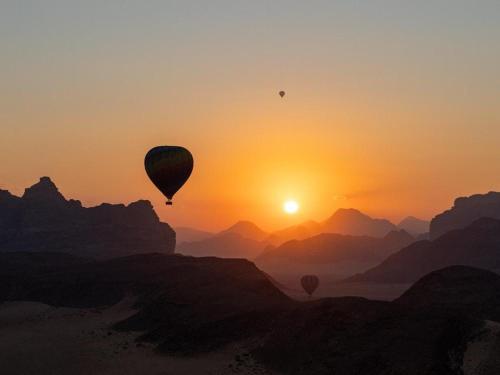 two hot air balloons flying over the mountains at sunset at Bubble RumCamp in Wadi Rum