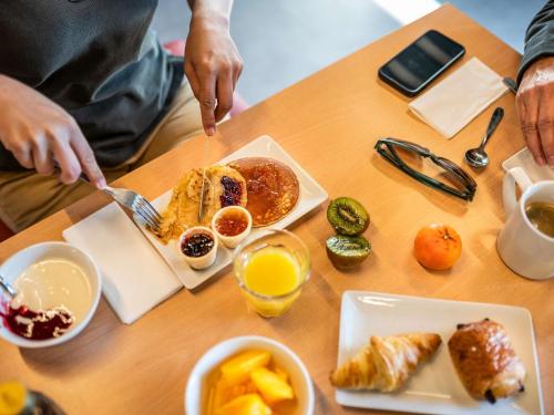 Eine Person isst ein Frühstück aus Pfannkuchen und Obst an einem Tisch. in der Unterkunft ibis Besançon Marchaux in Marchaux
