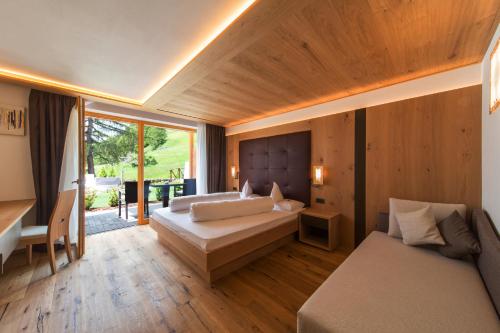 a bedroom with two beds and a desk and a couch at Hotel Fanes in Selva di Val Gardena