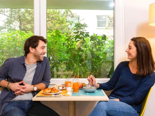 un homme et une femme assis à une table mangeant de la nourriture dans l'établissement Aparthotel Adagio Access La Défense - Léonard De Vinci, à Courbevoie