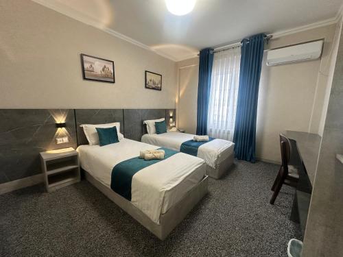 2 bedden in een hotelkamer met blauwe gordijnen bij Boston Hotel in Yakkasaray