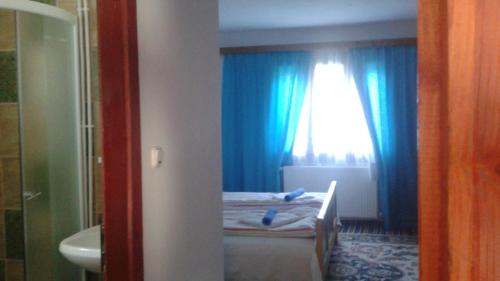 Schlafzimmer mit einem Bett und einem Fenster mit blauen Vorhängen in der Unterkunft Pensiunea Letitia in Suceviţa