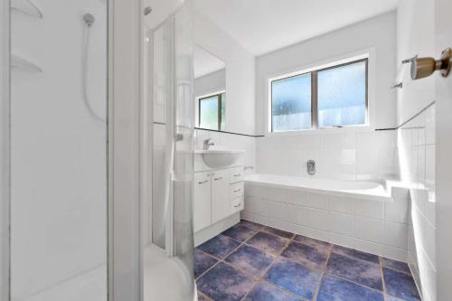 a white bathroom with a tub and a sink at Sweet North Cote Stay in Auckland