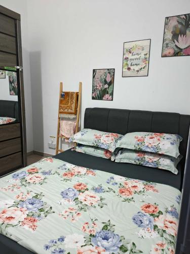 a bed with a floral bedspread and pillows on it at Aiman's Rose HomeStay in Teluk Panglima Garang