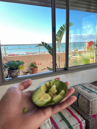 una persona che tiene in mano un avocado di fronte a una spiaggia di Room a Imsouane