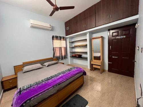 a bedroom with a bed with purple sheets and wooden cabinets at MUBSS Homestay in Tiruchirappalli