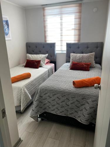1 Schlafzimmer mit 2 Betten und orangefarbenen Kissen in der Unterkunft Dep al costado del hospital- cercano a safari - buena accesibilidad a carretera panamericana 5 - parking privado in Rancagua