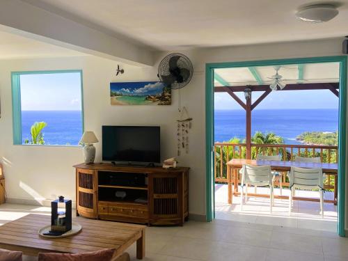 ein Wohnzimmer mit Fernseher und Balkon mit Meerblick in der Unterkunft Espace Harmonie Deshaies - Vue Mer & Piscine Panoramique in Deshaies