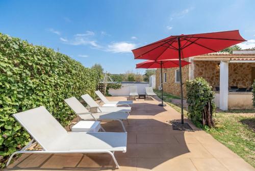a row of white lounge chairs and an umbrella at Es Marroig Villa y Spa in Llucmajor