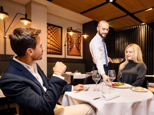 twee mannen en een vrouw aan een tafel in een restaurant bij Novotel Parma Centro in Parma