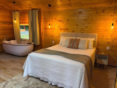 a bedroom with a bed and a tub in a wooden wall at Chalés Canto da Serra in Monte Verde