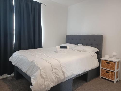 a bedroom with a bed with a gray headboard and curtains at Cosy Cottage in Ruakaka