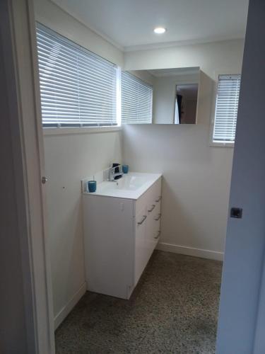 a white bathroom with a sink and two windows at Cosy Cottage in Ruakaka