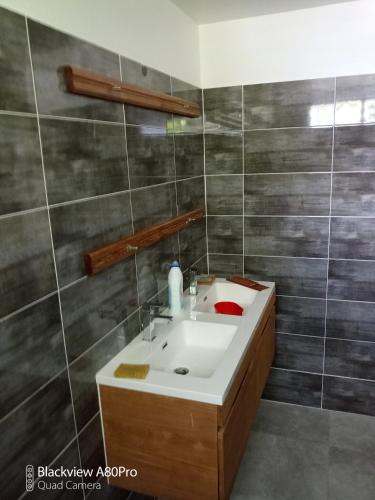 a bathroom with a white sink and gray tiles at kaz a gabou in Sainte-Rose