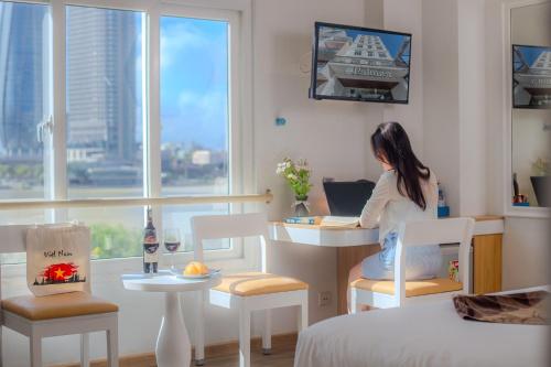 岘港Palmier Hotel - Art House Da Nang的坐在桌子上的女人,在房间里拿着笔记本电脑