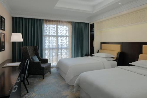 a hotel room with two beds and a chair at Sheraton Sharjah Beach Resort and Spa in Sharjah