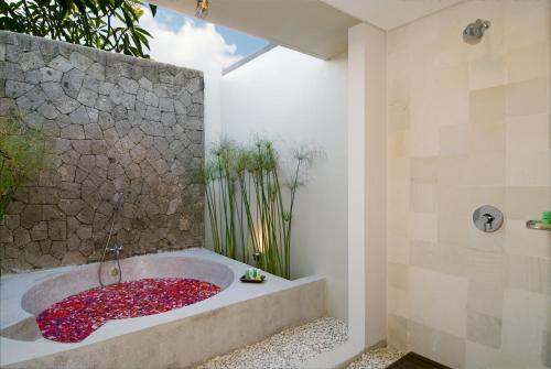 a bathroom with a bathtub with red flowers in it at Bumi Linggah Villas Bali in Sukawati