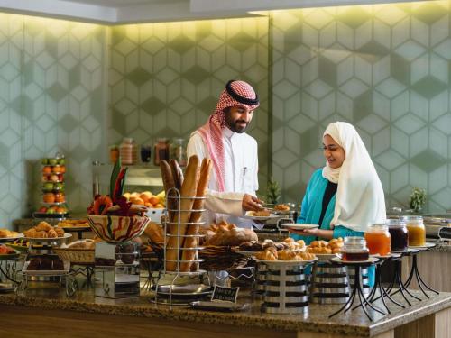 Ein Mann und eine Frau bereiten Essen am Buffet vor. in der Unterkunft ibis Styles Makkah in Mekka