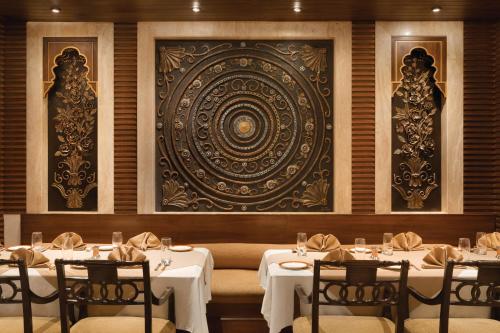 a dining room with white tables and chairs and a wall at Ramada Plaza by Wyndham JHV Varanasi in Varanasi