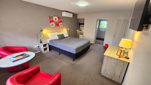 een slaapkamer met een bed, een tafel en rode stoelen bij Carramar Motor Inn in Palmerston North
