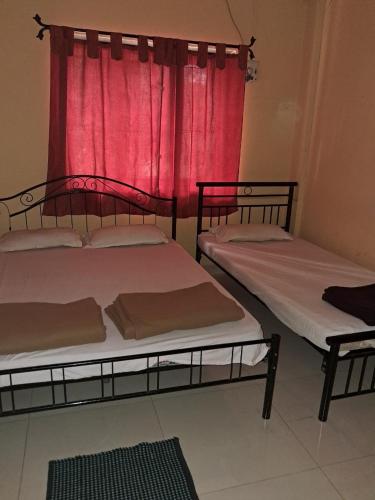 two beds in a room with a red curtain at Hotel Cosy Nook in Malvan