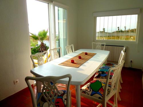 a dining room table with white chairs and a white table at Vila Mar in Porto Covo