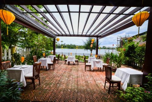 a restaurant with tables and chairs and a view of the water at Villa Orchid Garden Riverside Hoi An in Hoi An