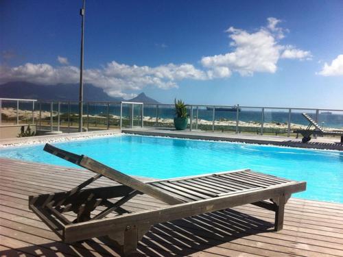 a swimming pool with a bench next to the ocean at Beachfront Apartment at Seaspray in Blouberg in Bloubergstrand