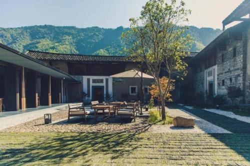 a patio with a table and chairs and a tree at Tsingpu Tulou Retreat 青普文化行馆 南靖土楼店 in Futian