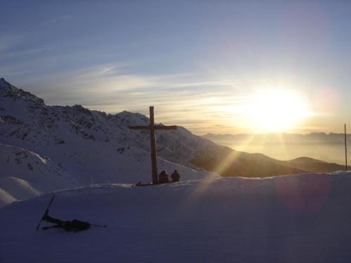 a cross on top of a snow covered mountain with the sun at Gîte Le Cerf de Belledonne in Sainte-Agnès