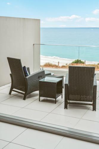 three wicker chairs and a table on a balcony at Entice at Hyams - pet-friendly beachfront home in Hyams Beach