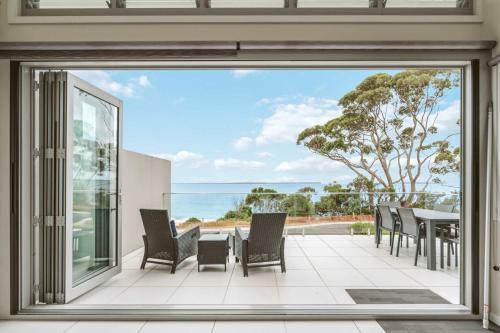 a patio with a table and chairs and a view of the ocean at Entice at Hyams - pet-friendly beachfront home in Hyams Beach