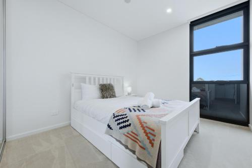 a white bedroom with a white bed and a window at Luxury 2BR Stay near Olympic Park Parramatta FREE Parking in Sydney