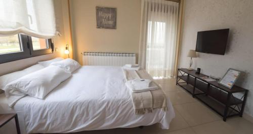 een slaapkamer met een wit bed en een televisie bij Apartamentos Monte Hernanz in Riaza