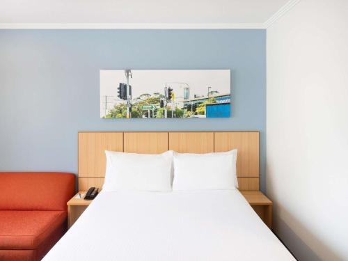 - une chambre avec un lit et un canapé orange dans l'établissement Mercure Sydney Manly Warringah, à Sydney