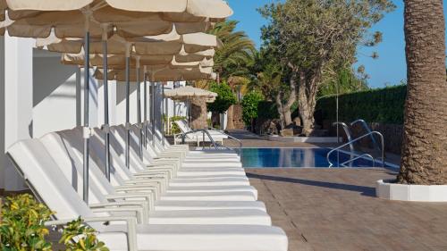 een rij witte stoelen onder een parasol naast een zwembad bij Boutique Hotel H10 White Suites - Adults Only in Playa Blanca