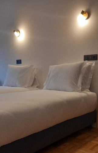 een bed met witte kussens en 2 verlichting aan de muur bij Lavanda Termas de São Pedro do Sul in Termas de Sao Pedro do Sul