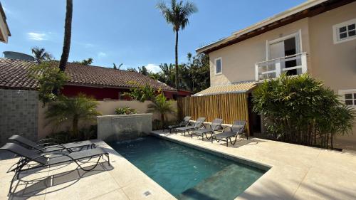 a swimming pool with chairs and a house at Pousada Pantai Maresias in Maresias