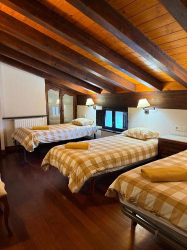 three beds in a room with wooden ceilings at Albergue Rural Montebaserria in Ziortza-Bolibar