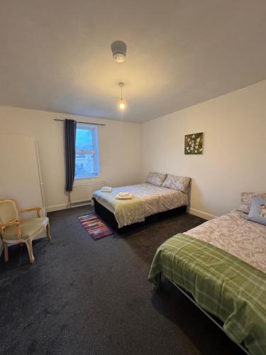 a bedroom with two beds and a chair and a window at NextDoor Morden in Merton