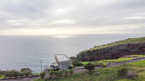 a house on a cliff next to the ocean at Sunshine Villa with Optionally Heated Pool 150m above Ocean & Sandy Beach in Estreito da Calheta