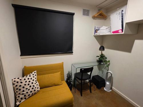 a living room with a yellow couch and a large screen at A Sweet Studio for One in Altona