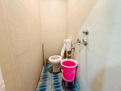 a bathroom with a toilet and a pink bucket at Hotel Tathastu Inn in Ujjain
