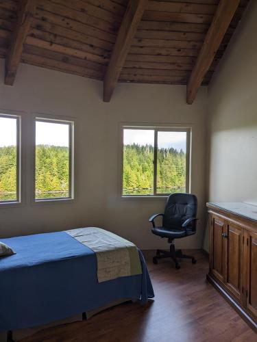 a bedroom with a bed and a chair and windows at Argo's Landing in Bamfield