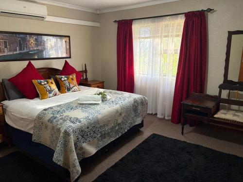 een slaapkamer met een bed en een raam met rode gordijnen bij Waaigras in Brackenfell