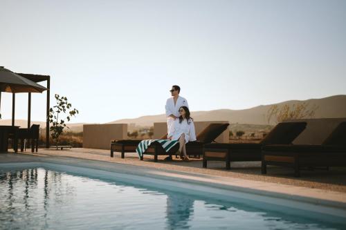 a man and woman sitting on a bench next to a swimming pool at Equ Hotel Boutique in El Porvenir