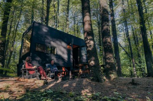 Twee mensen zitten voor een klein zwart huisje in het bos. bij Postcard Cabins Eastern Catskills, Outdoor Collection by Marriott Bonvoy in Catskill
