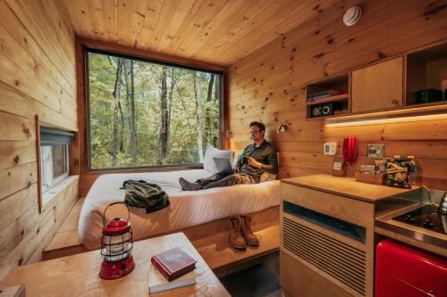 een man zittend op een bed in een klein huisje bij Postcard Cabins Eastern Catskills, Outdoor Collection by Marriott Bonvoy in Catskill