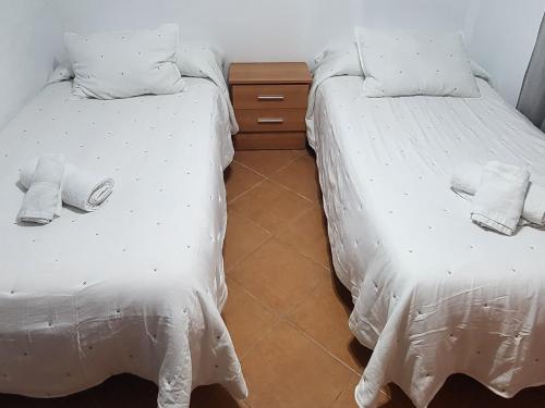 two beds with white sheets and a wooden night stand at Casa Curro in Benaocaz