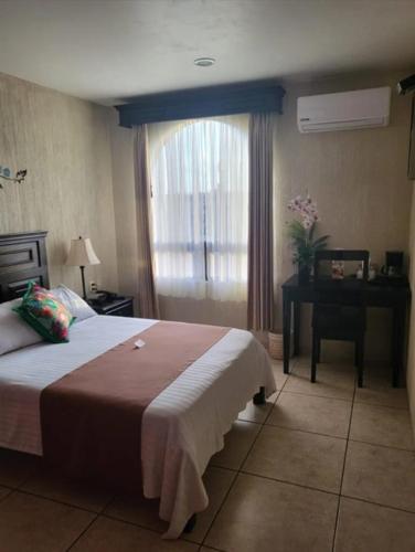a bedroom with a bed and a desk and a window at Hotel Villalba in Comitán